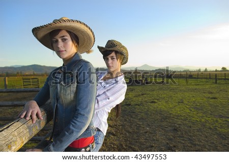 Twin Cowgirls at sunset leaning against a wood fence