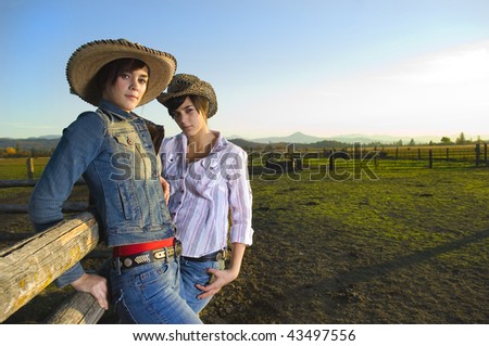 Twin Cowgirls at sunset leaning against a wood fence