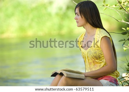 Young woman reading bible by river in summer