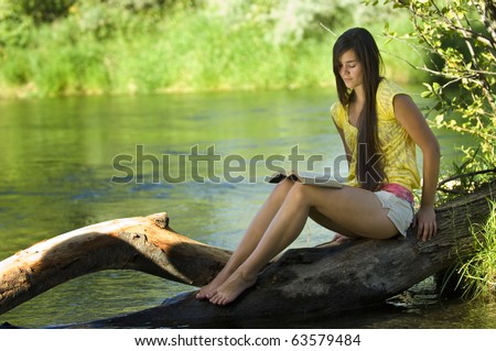 Young woman reading bible by river in summer