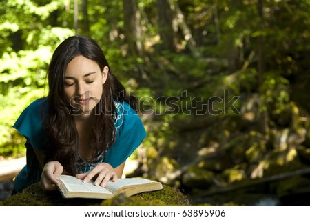 Young woman reading bible by stream in summer