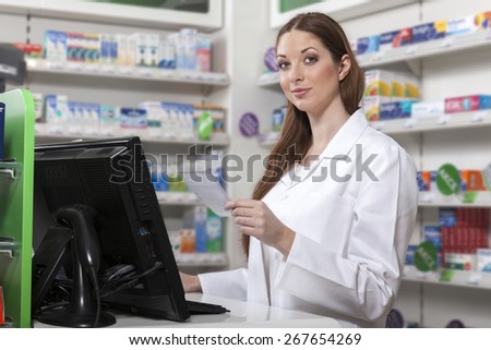 Attractive pharmacist in the pharmacy at the computer holds prescription