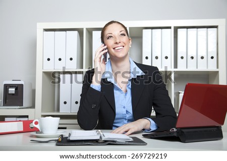Businesswoman makes a call on her cell phone sitting at her desk