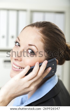 Friendly business lady sits at her desk while looking over her shoulder having a phone call