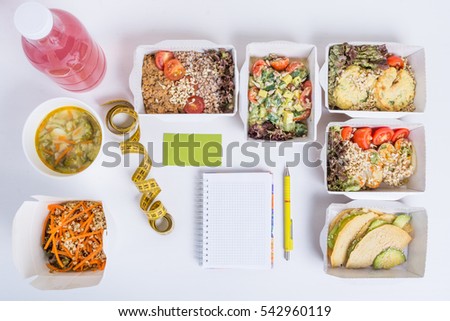 Healthy nutrition plan. Fresh daily meals delivery. Restaurant food for one, vegetable, meat and fruits in foil boxes, detox water, business card, notebook and pencil on white background.