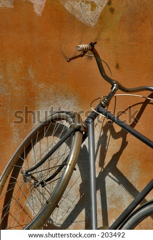 Old bicycle resting against a contrasting orange wall with a shadow