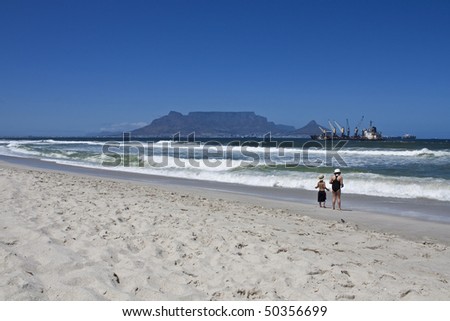 Two children stand alone on the beach at Bloubergstrand in South Africa, facing Table Mountain.