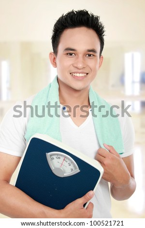 Young fitness man carrying a weight scale in a gym