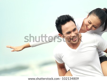 Close up portrait of a young asian man giving piggyback to woman on the beach.