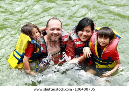 Cheerful family in the water wearing life vest smiling at camera
