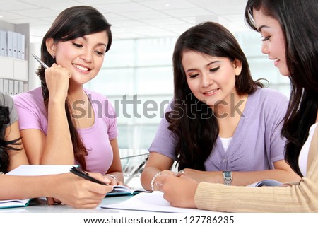 Studying happy young woman reading her book for school together with friends