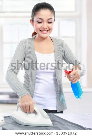 Happy young beautiful woman ironing clothes at home