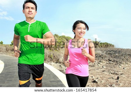 Sporty asian young couple jogging outside together on jogging track