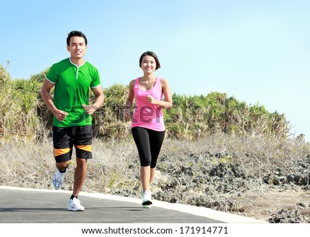 Sporty asian young couple running outside together on jogging track