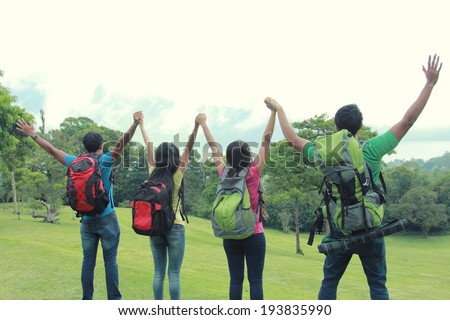 A group of friends on a hiking raise their hand together. shoot from behind