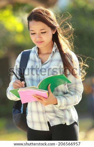 Girl writing something on the books in campus park