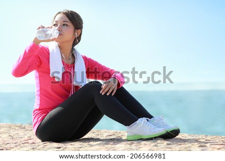Portrait of asian sporty fitness woman drinking a bottle of water while having a break