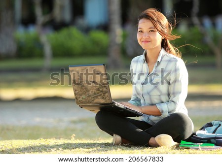 Young student sitting cross-legged on grass with laptop doing a homework
