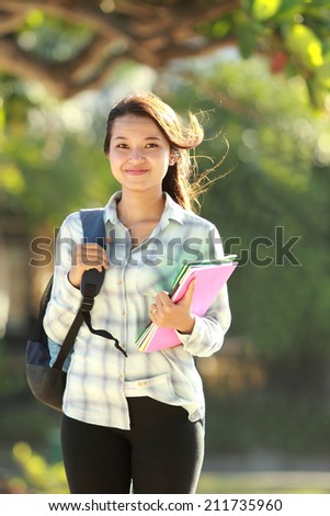 Portrait of beautiful young woman with bag and books walking in campus park