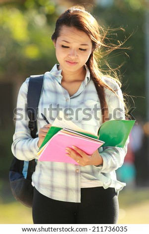 Portrait of beautiful young woman with bag and books in campus park