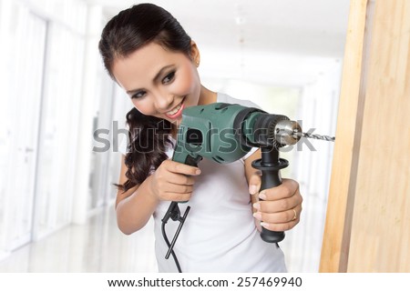 female wearing working clothes with toolbelt using electric drill