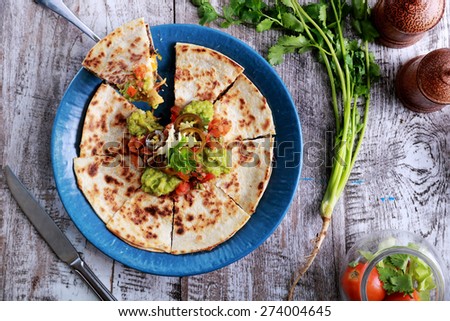 top view mexican cuisine quesadilla served at blue plate with guacamole, salsa and jalapenos