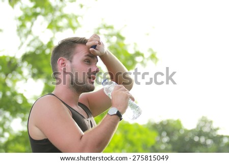 portrait of male runner wiping his sweat while holding a bottle of water during break after tired running