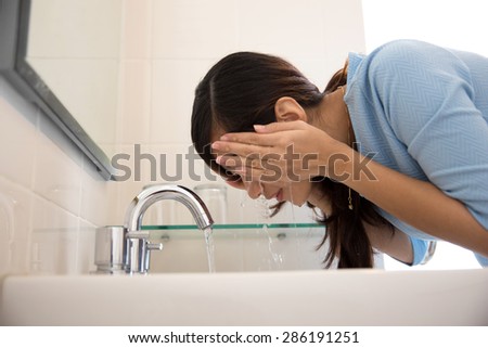 A portrait of an asian woman washing her face on the sink