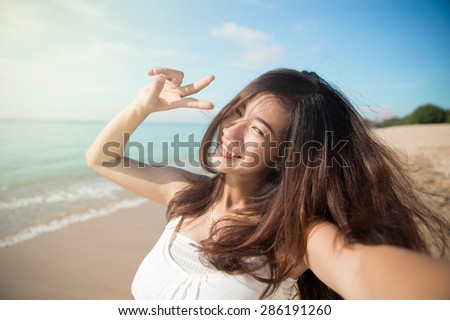 A portrait of a Happy young Asian woman take photos of her self, smile to camera, selfie. victory sign hand gesture
