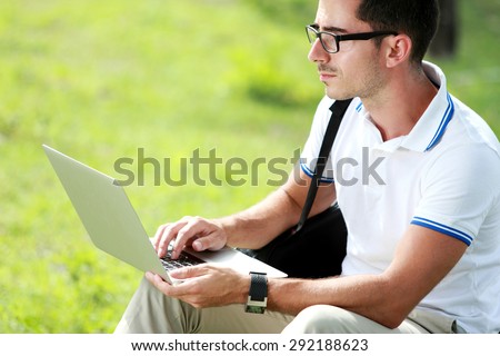 portrait of a college student sitting under the tree while studying using a laptop at college park