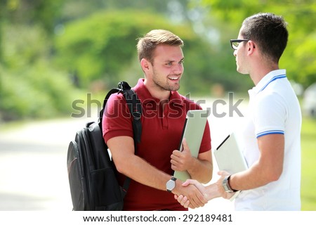 portrait of a college student with backpack happy to meet his friend and then shake hands