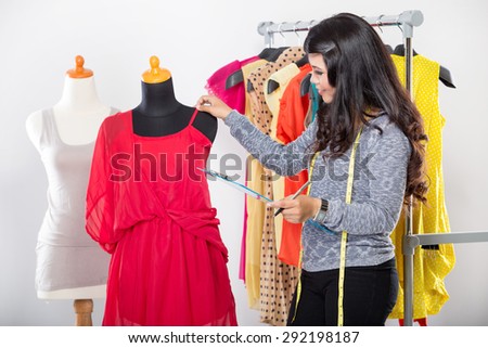 A portrait of a young asian designer hold fabric enrobing it to the mannequin, smiling