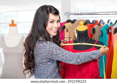 A portrait of a young fashion designer or Tailor working on a design or draft, she takes measure on a dressmakers dummy