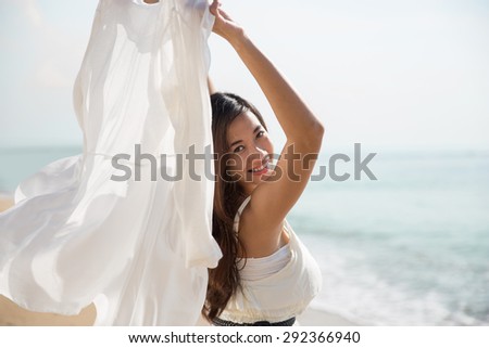A portrait of an Asian woman enjoying her time in the beach, closing her eyes and arms open wide