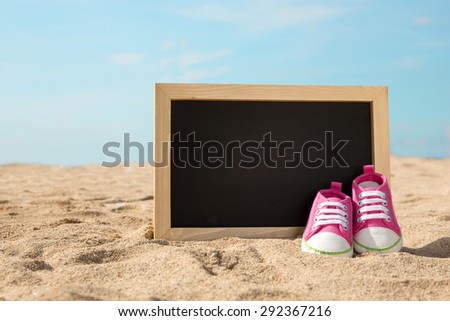 pair of toddler shoes and mini chalk board on the sand, beach concept background