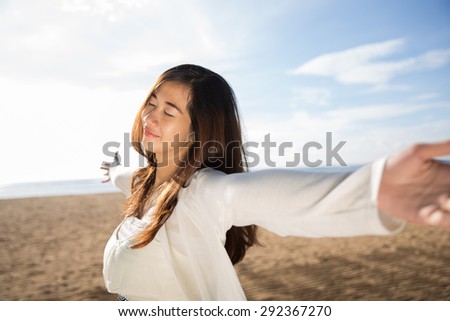 A portrait of an Asian woman enjoying her time in the beach, closing her eyes and arms open wide