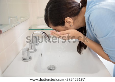 A portrait of an Asian woman washing her face on the sink