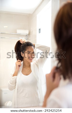 A portrait of a Beautiful asian woman tying her hair while smile at the mirror