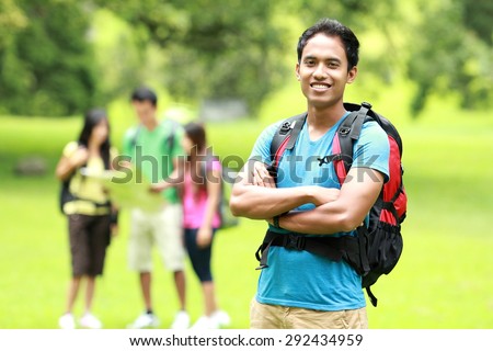 A portrait of handsome man backpacker and a group of asian youngers backpacking at the background