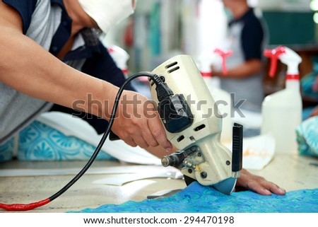 portrait of worker using cutting machine for cutting fabrics at textile factory