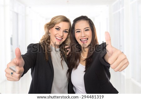 A portrait of a young business woman making thumbs up gesture wearing blouse and blazer.
