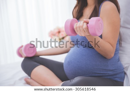 A portrait of a Beautiful asian pregnant woman doing exersice on her bed using dumbell