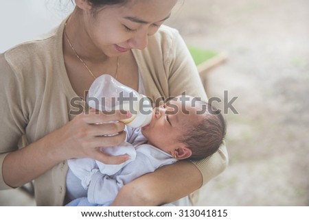 A portrait of cute newborn baby being fed by her mother using bottle