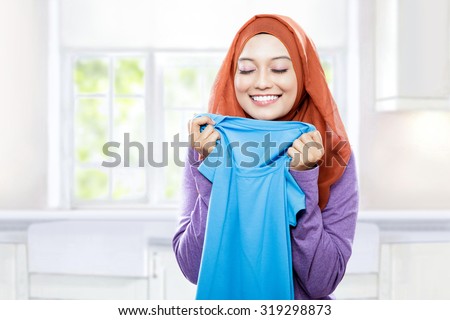 portrait of young woman wearing hijab holding and smelling the fresh clean laundry