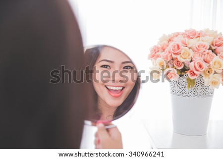 Woman holding a mirror, smiling brightly looking at her face