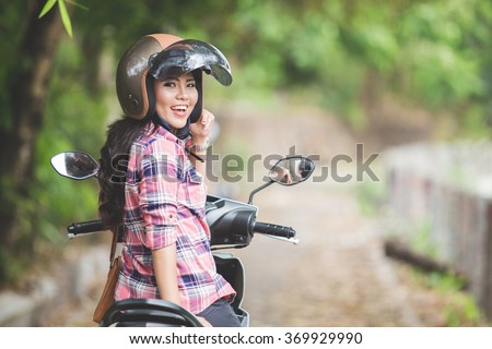 A portrait of a young asian woman riding a motorcycle in a park