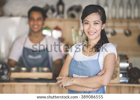 Successful small business owner standing with crossed arms with partner at the background