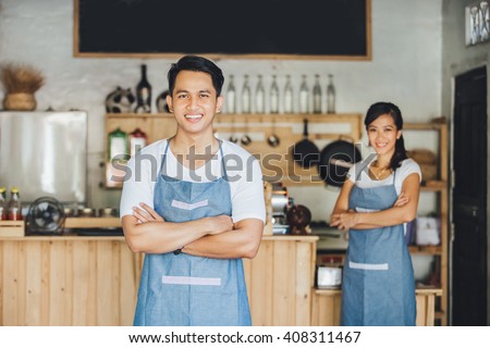 Successful small business owner standing with crossed arms with partner at the background