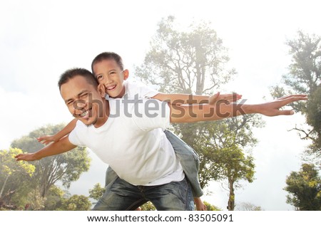 father giving his son piggyback ride outdoors against sky