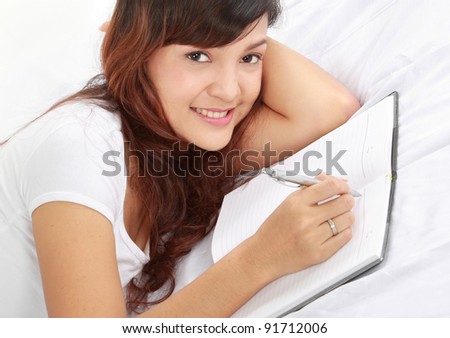 Closeup portrait of a smiling young girl writing book while lying on the bed